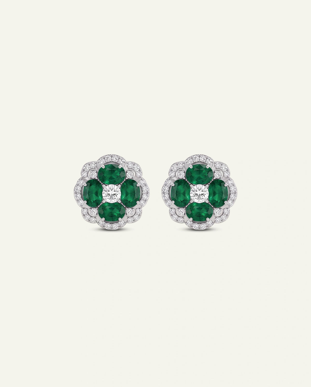 A pair of floral stud earrings featuring four green emerald-cut gemstones in a silver-toned setting, surrounded by a halo of small clear stones, centered on a light cream background.