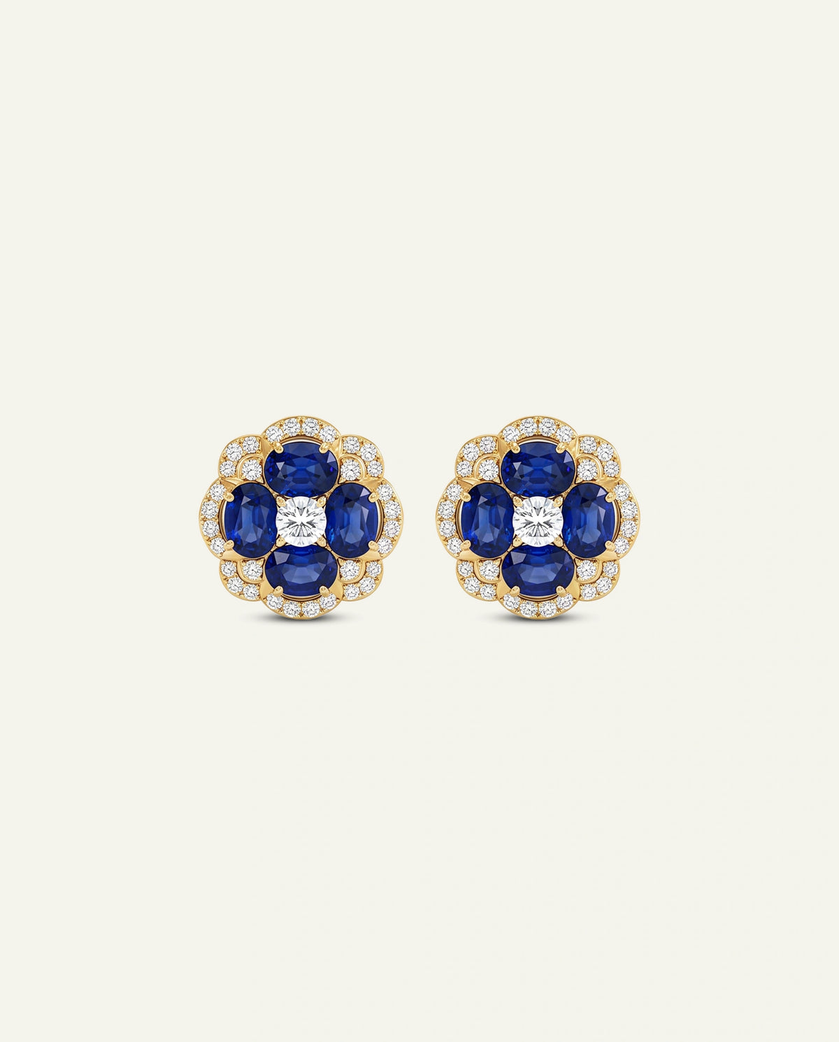 A pair of gold floral stud earrings featuring four deep blue sapphires and a central round diamond surrounded by small clear stones, set against a light cream background.