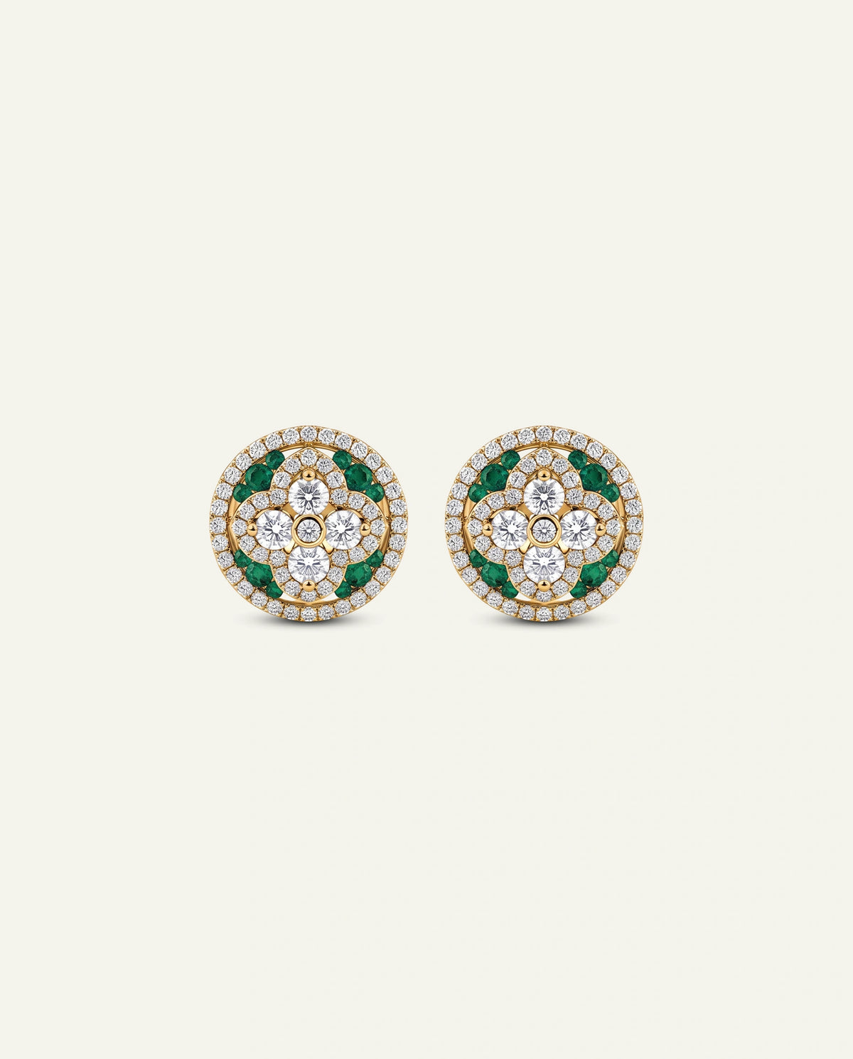 A pair of round gold stud earrings decorated with clear pavÃ©-set stones and green emerald-cut accents, displayed on a light cream background.