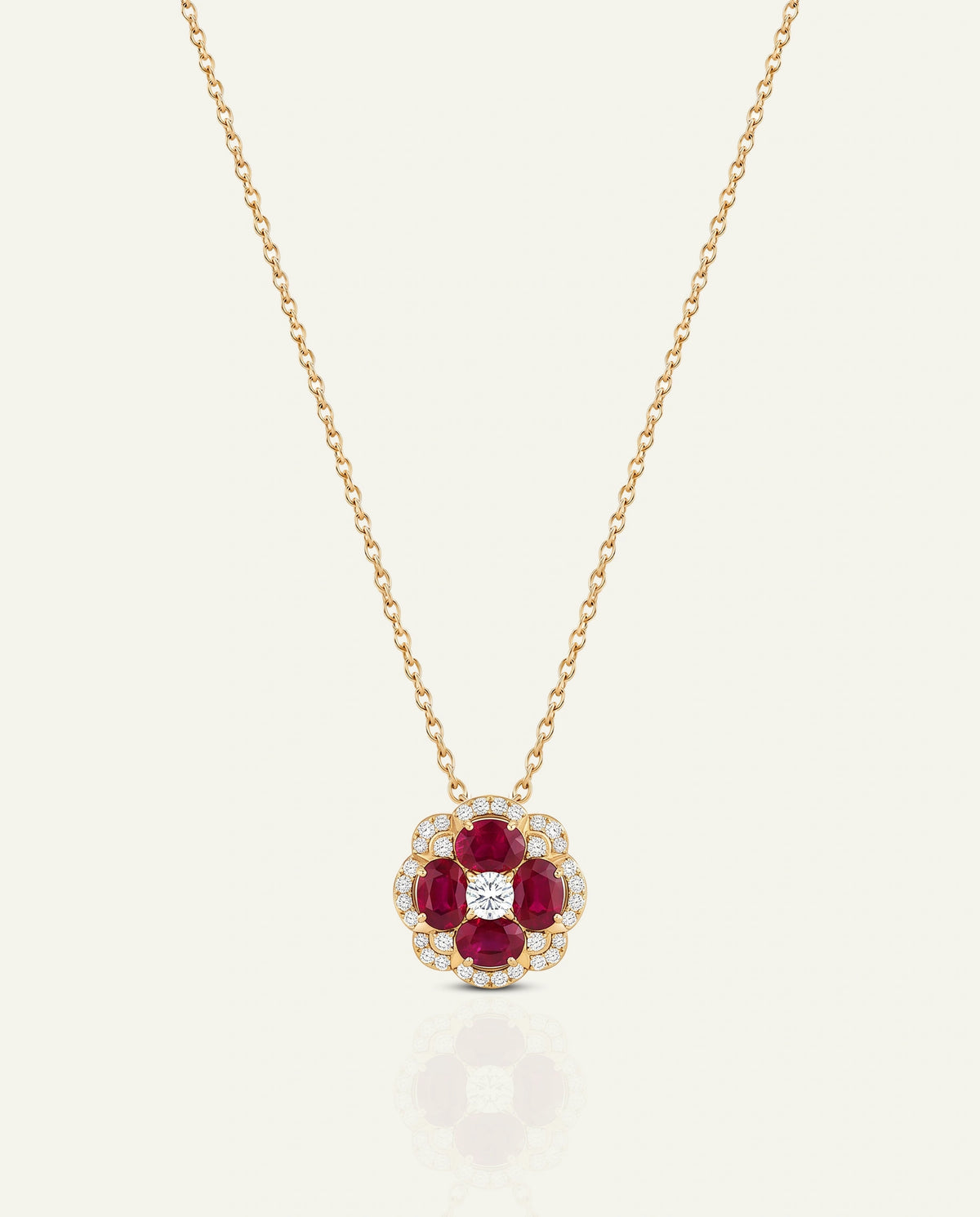 A gold chain necklace with a flower-shaped pendant featuring deep red round gemstones and a small clear center stone, shown on a light cream background.