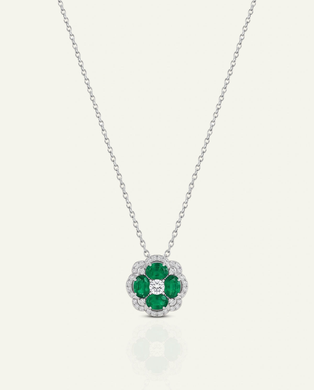 A silver-tone floral pendant necklace featuring five green emerald-cut stones in a halo-like arrangement with a small clear center stone, suspended from a delicate silver chain on a light cream background.