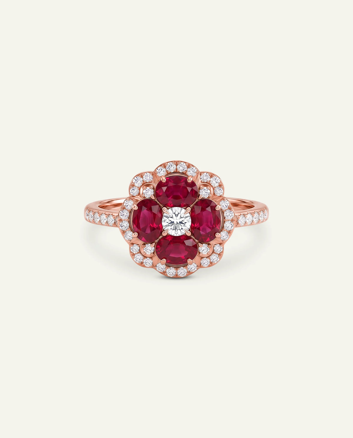 A rose gold ring featuring a flower-shaped cluster with four round-cut deep red rubies, a single round-cut clear center stone, and a halo of small clear stones, set against a plain off-white background.