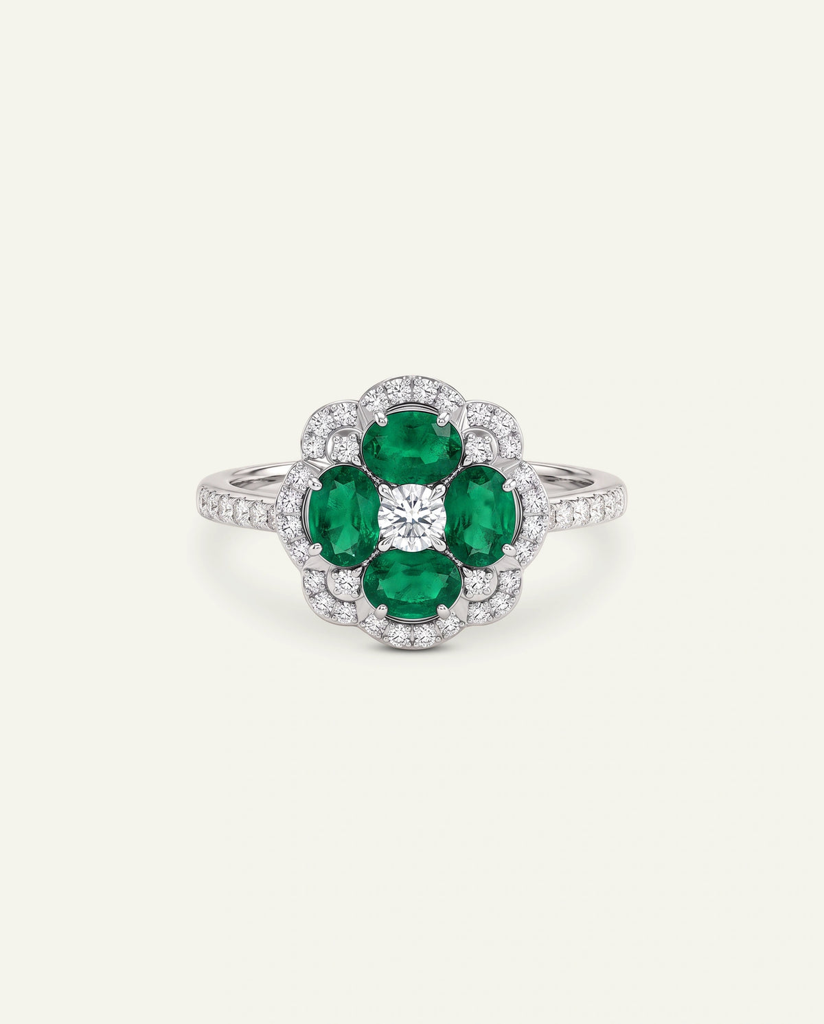 A floral cluster ring featuring four oval-cut green emeralds and a central round brilliant-cut diamond, surrounded by a halo of small pavÃ©-set diamonds on a silver-toned band, set against a solid off-white background.