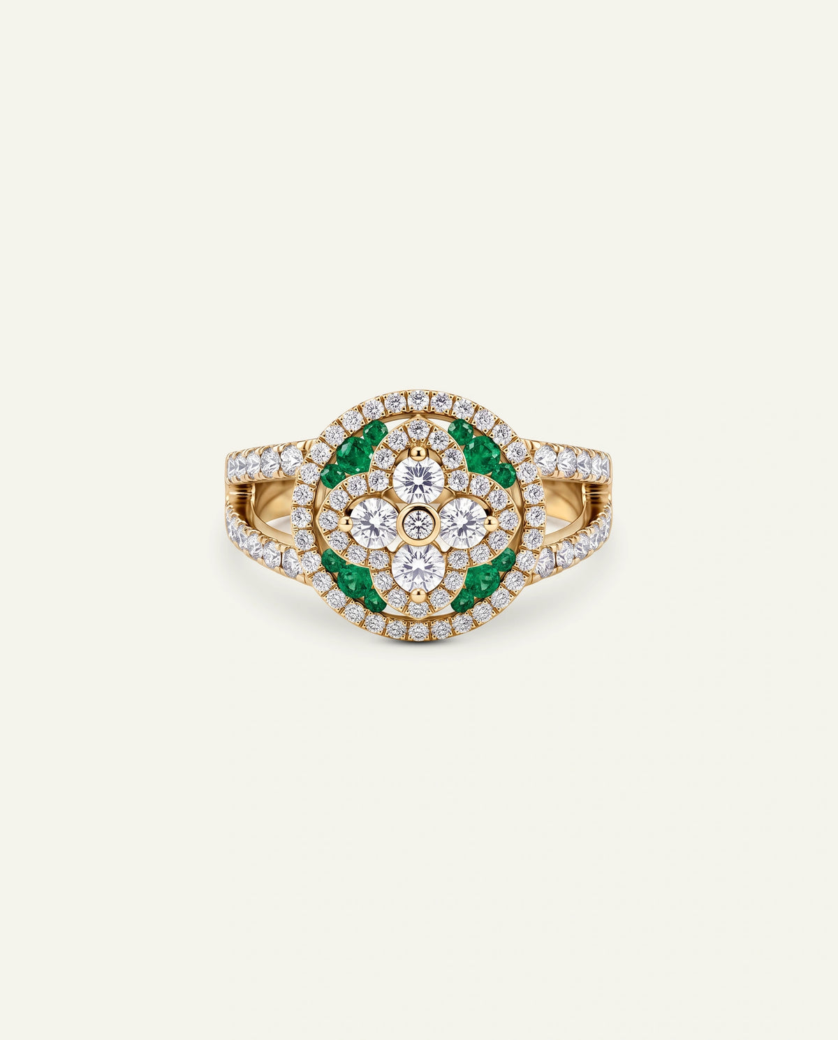 A yellow gold ring featuring a circular floral cluster with green emerald-cut stones and clear pavÃ©-set diamonds, centered on a light cream background.