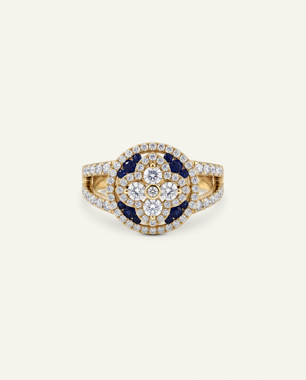 A gold ring featuring a central floral cluster of dark blue sapphires and clear diamonds, surrounded by a halo of small diamonds, on a light cream background.