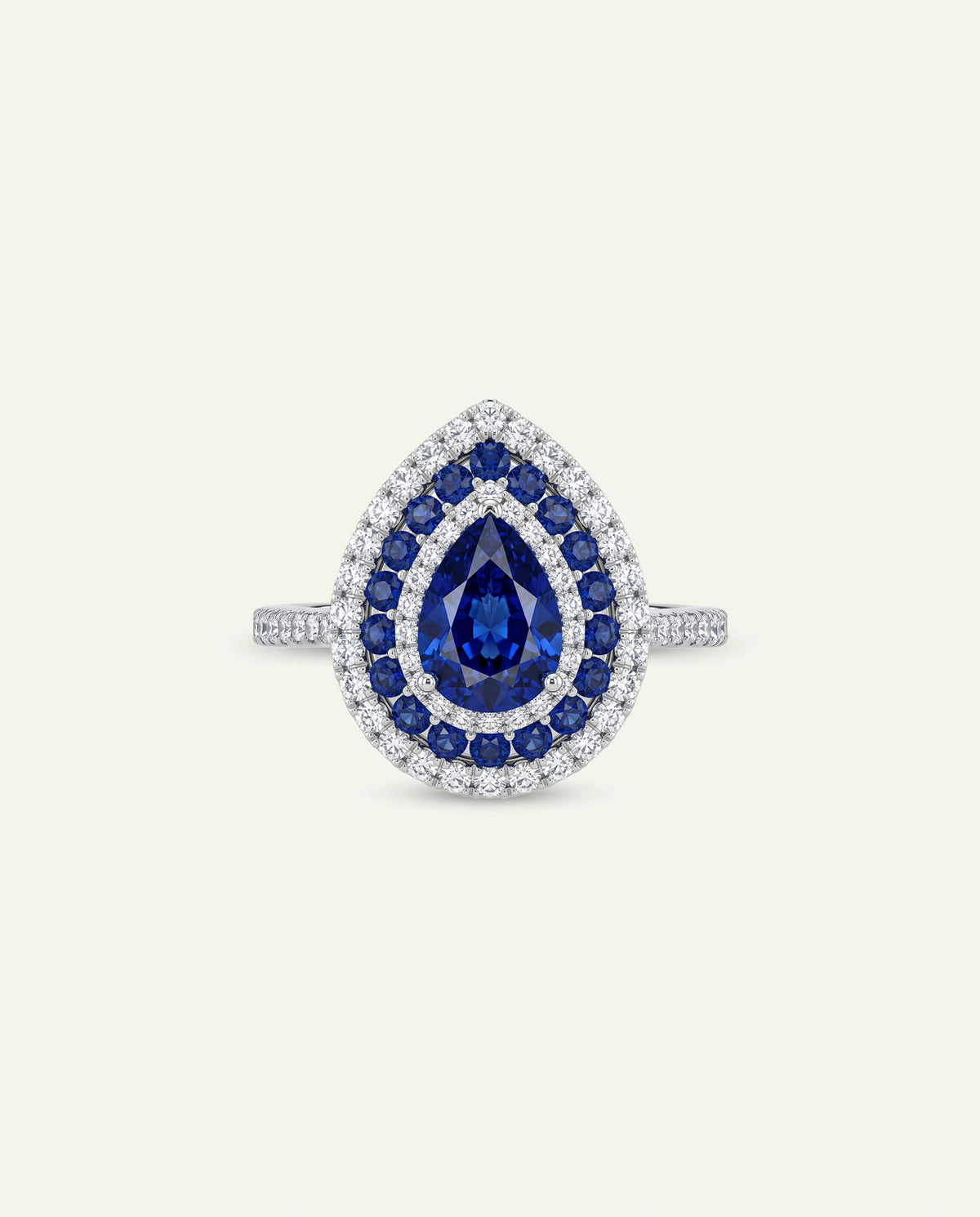 A pear-shaped halo ring featuring a central deep blue sapphire surrounded by smaller blue sapphires and clear stones, set on a silver-toned band against a light cream background.