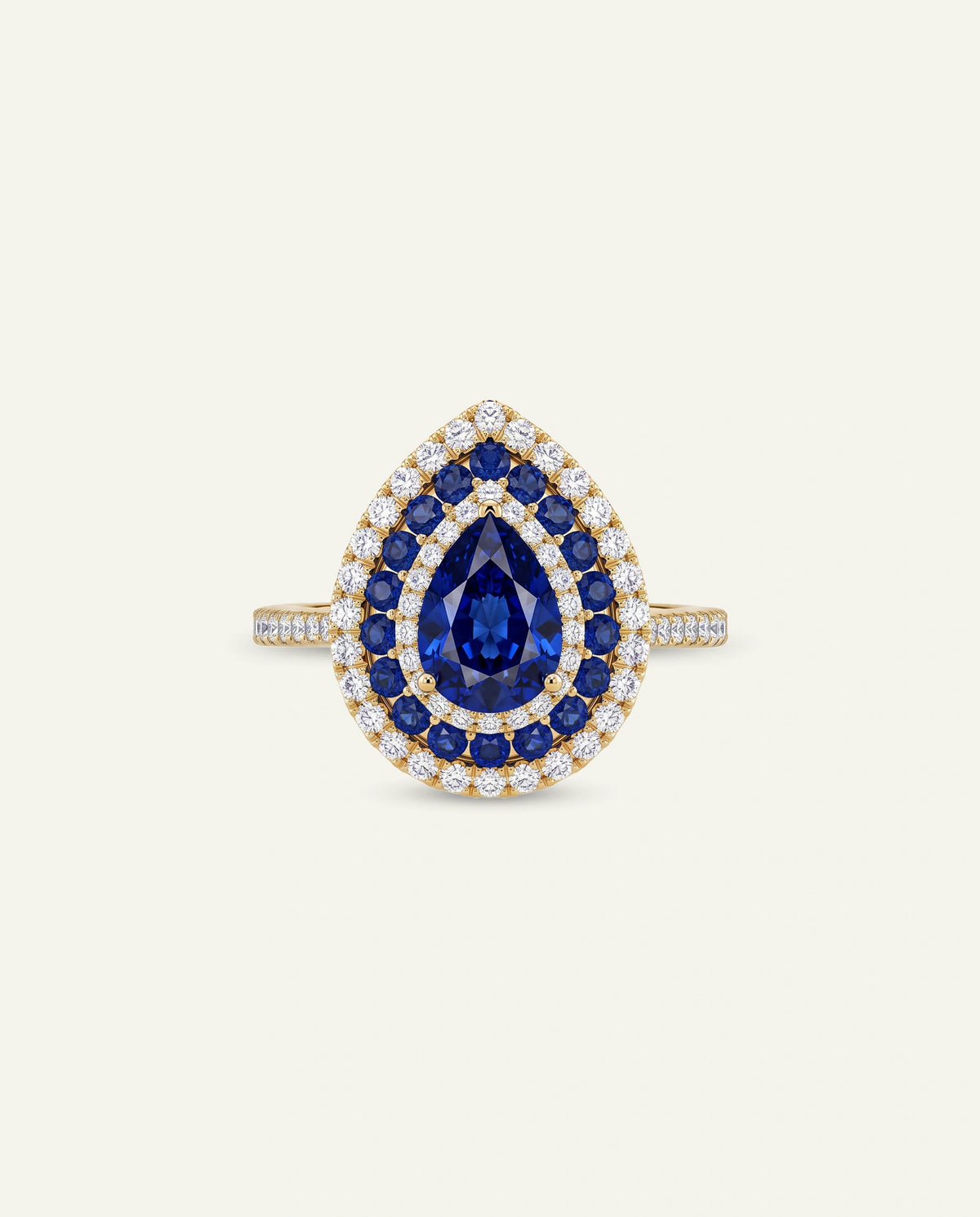 A teardrop-shaped ring featuring a central deep blue sapphire surrounded by double halos of small clear stones, set in yellow gold on a light cream background.