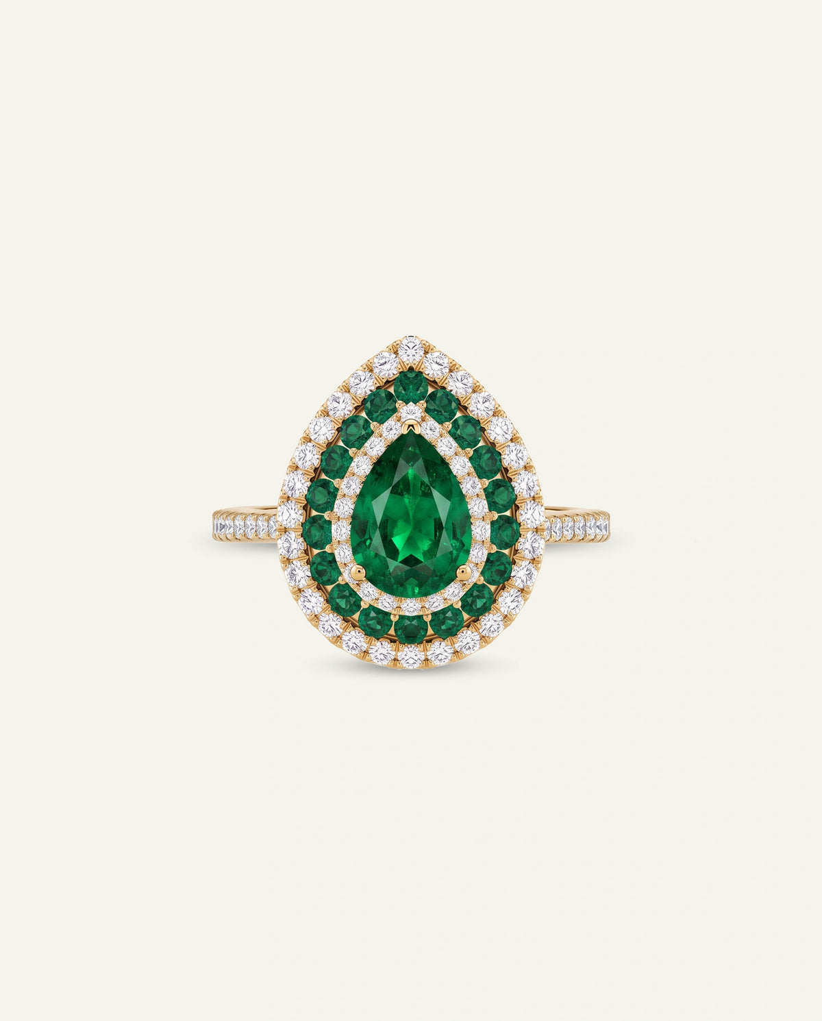 A pear-shaped emerald-cut ring featuring a central green emerald surrounded by double halos of small white stones and a border of round green stones, set in yellow gold on a light cream background.