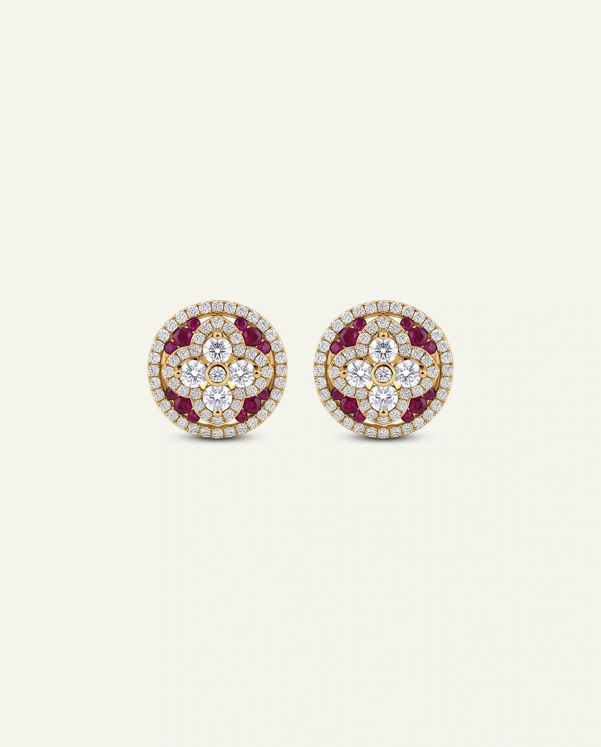 A pair of round gold stud earrings set with clear crystals and deep red gemstones, displayed on a light cream background.