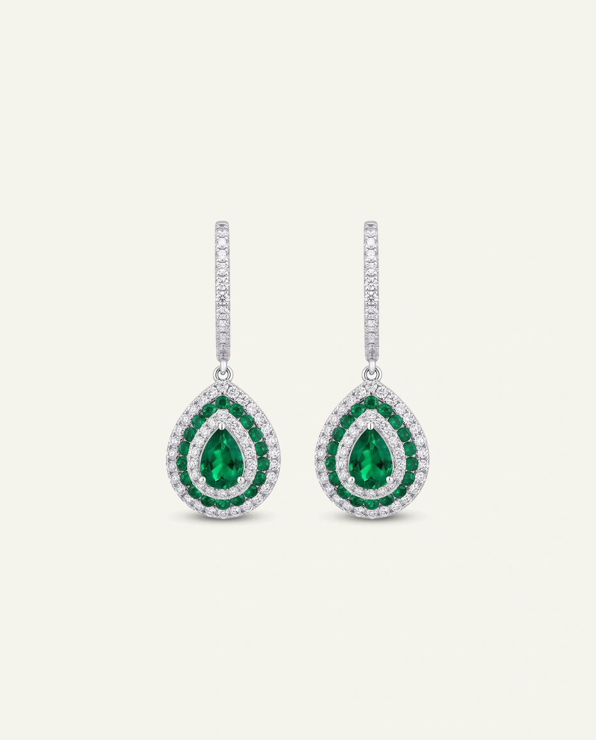A pair of teardrop-shaped drop earrings featuring green emerald-cut center stones surrounded by double rows of small clear stones, suspended from vertical bars of clear stones, set against a light cream background.
