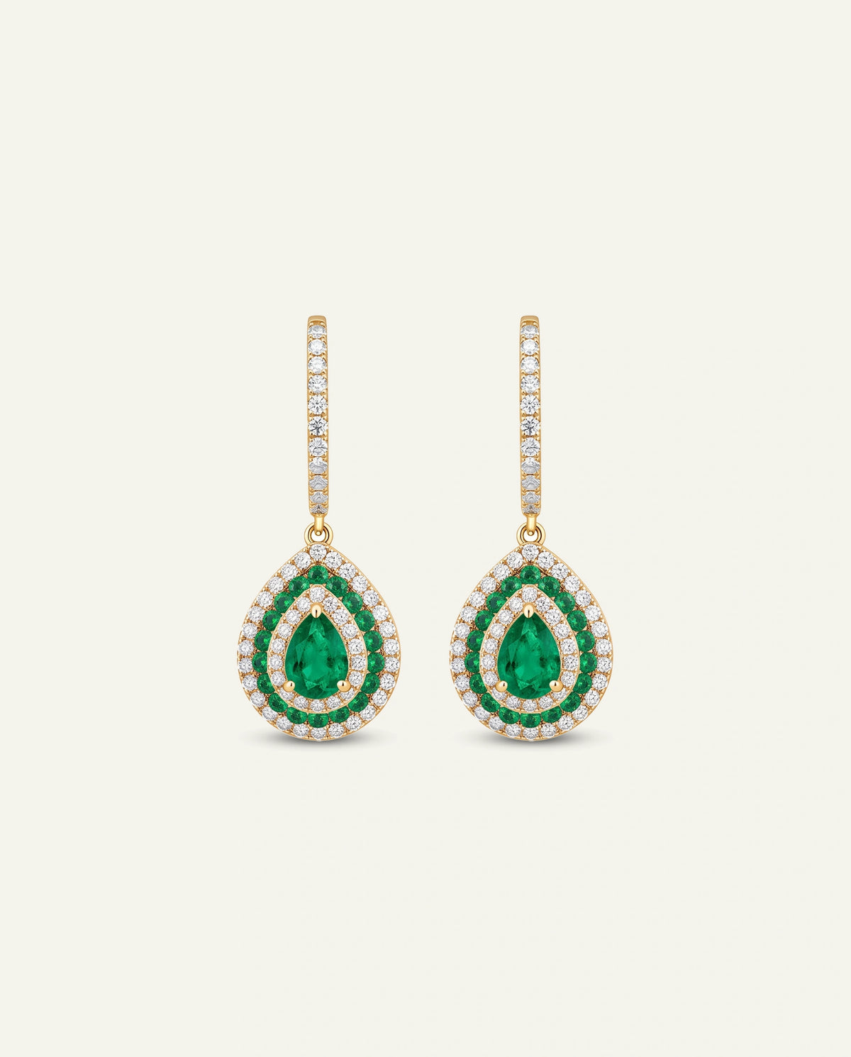 A pair of gold drop earrings featuring pear-cut emerald green stones surrounded by small clear stones, shown on a light cream background.