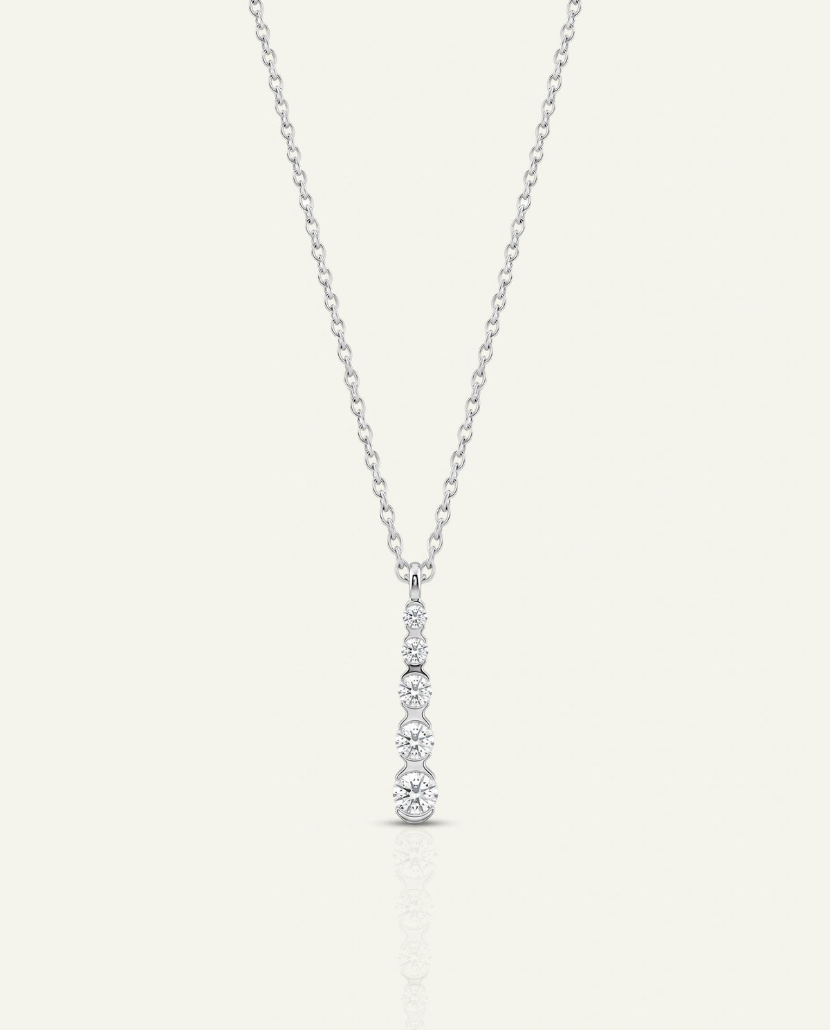 A delicate silver-toned necklace with a vertical drop pendant set with clear gemstones, displayed on a light cream background.