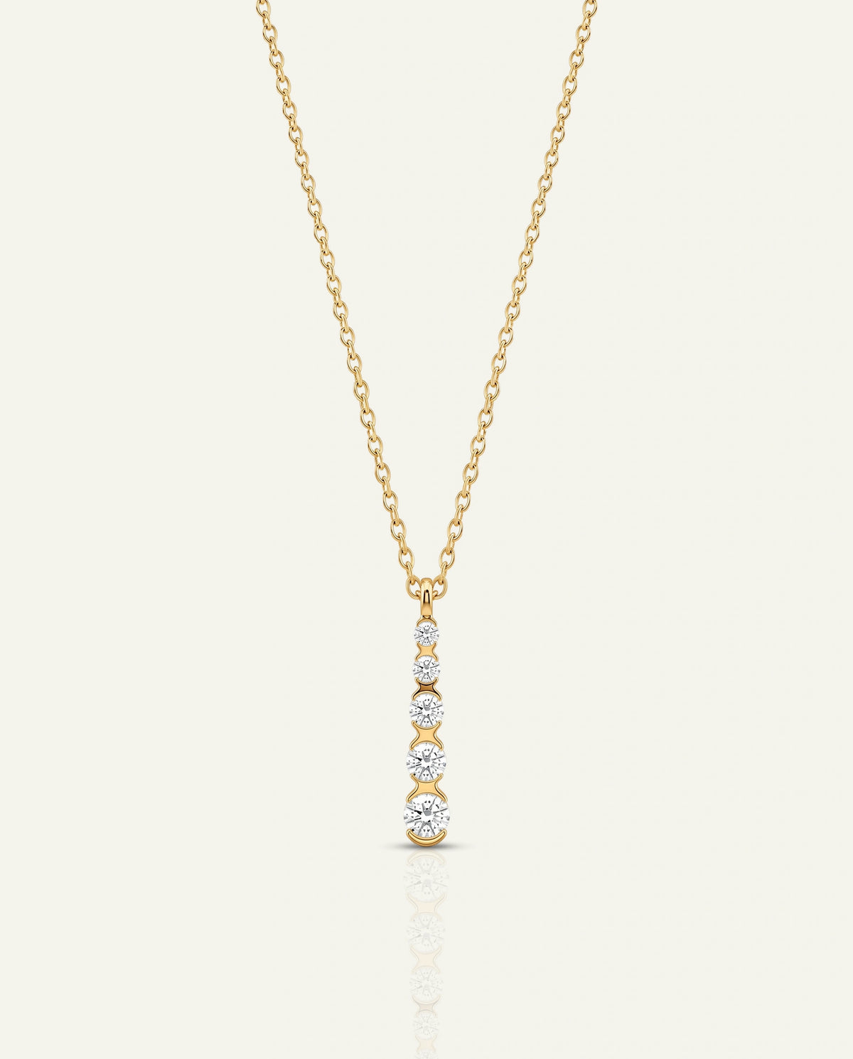 A delicate yellow gold chain necklace with a vertical pendant featuring three bezel-set clear round gemstones on a light cream background.