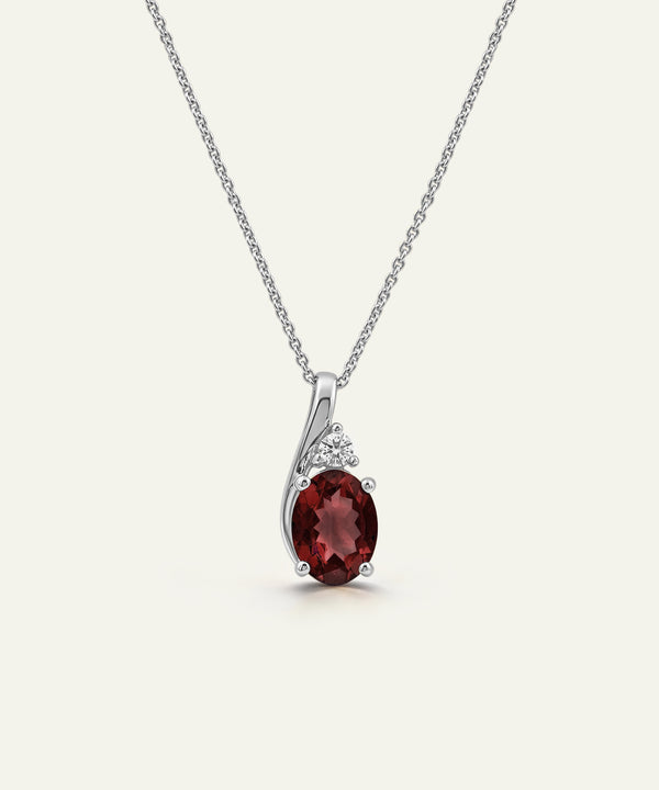 A silver pendant necklace featuring an oval deep red gemstone and small clear accent stones, displayed on a clean off-white background.