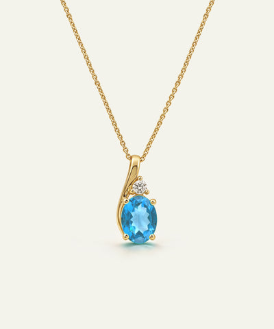 A gold necklace with a pendant featuring an oval-cut light blue gemstone and a small clear accent stone, shown on a plain light background.