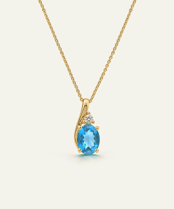 A gold necklace with a pendant featuring an oval-cut light blue gemstone and a small clear accent stone, shown on a plain light background.