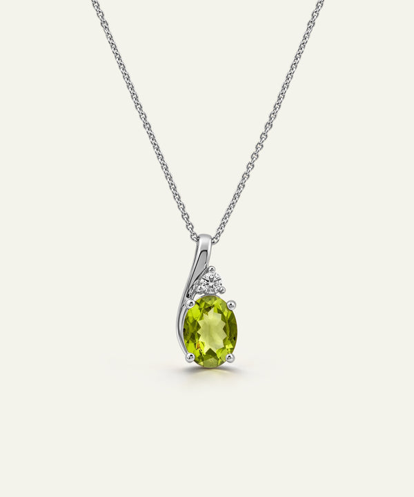 A silver pendant necklace featuring an oval-cut lime green peridot gemstone, accented by small round clear stones in a curved silver setting, suspended from a delicate silver chain against a light cream background.