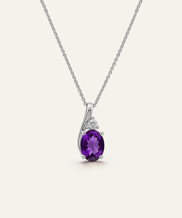 A silver pendant necklace featuring an oval-cut purple amethyst center stone, accented by small clear stones in a curved silver setting, suspended from a delicate silver chain against a light cream background.