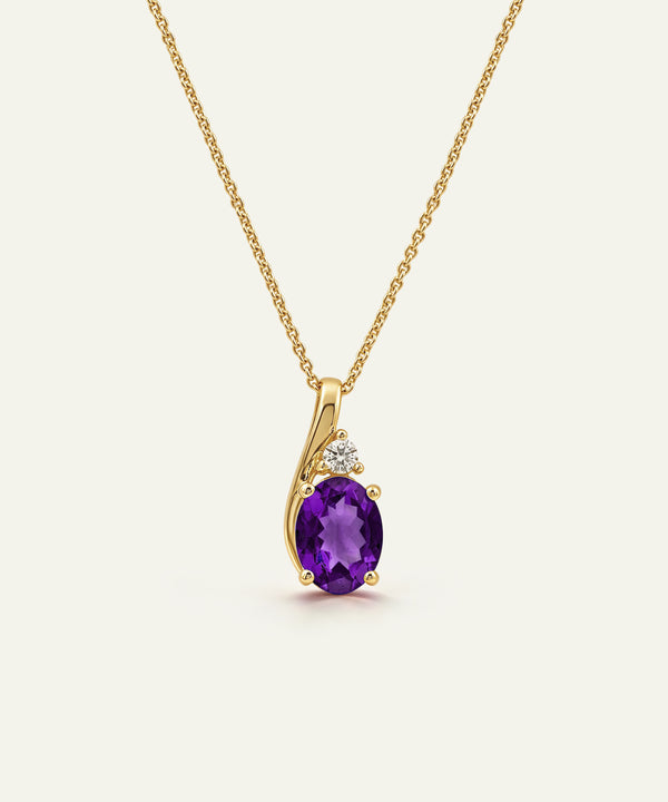A gold pendant necklace featuring an oval-cut purple amethyst center stone and a small clear accent stone, shown on a delicate gold chain against a light cream background.