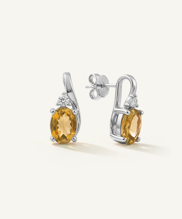 A pair of silver drop earrings featuring oval-cut yellow citrine gemstones and small clear accent stones, shown on a clean off-white background.