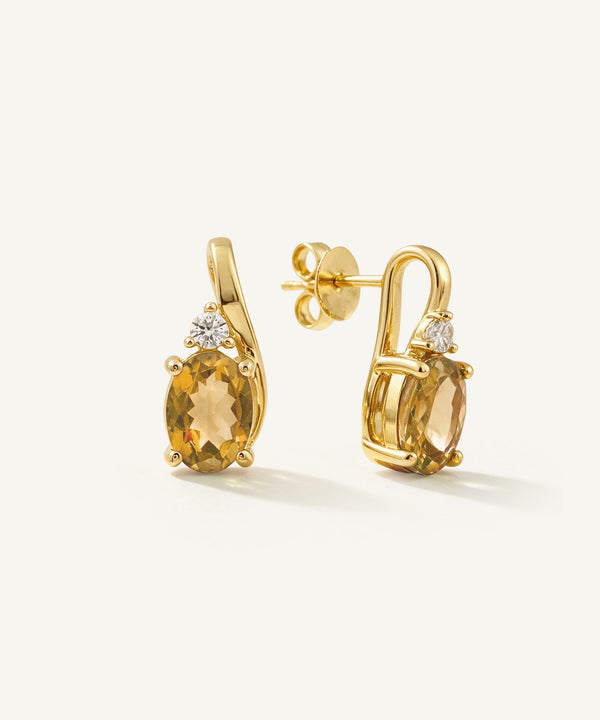 A pair of gold drop earrings featuring oval yellow citrine gemstones and small clear accent stones, displayed on a clean off-white background.