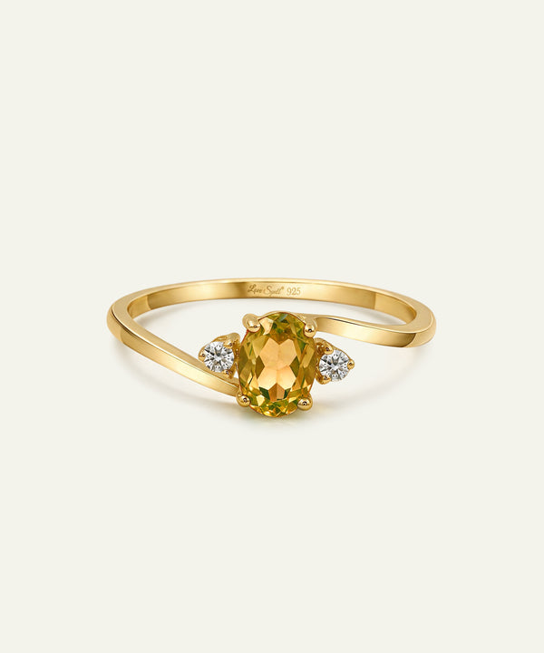 A yellow gold ring featuring an oval-cut green peridot center stone and two small round-cut clear diamonds on either side of the band, set against a light off-white background.