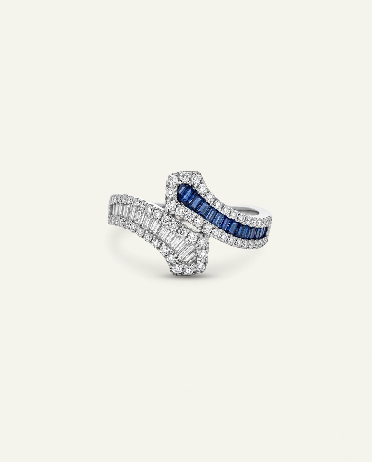 A silver-toned ring featuring a split design with baguette-cut clear stones and a central channel of deep blue sapphires, set against a solid off-white background.
