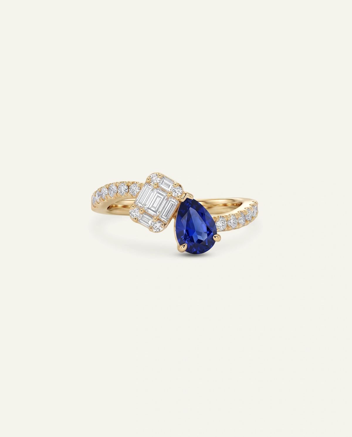 A gold ring featuring a pear-cut blue sapphire center stone, an emerald-cut clear diamond, and a curved shank paved with small clear diamonds, set against a solid off-white background.
