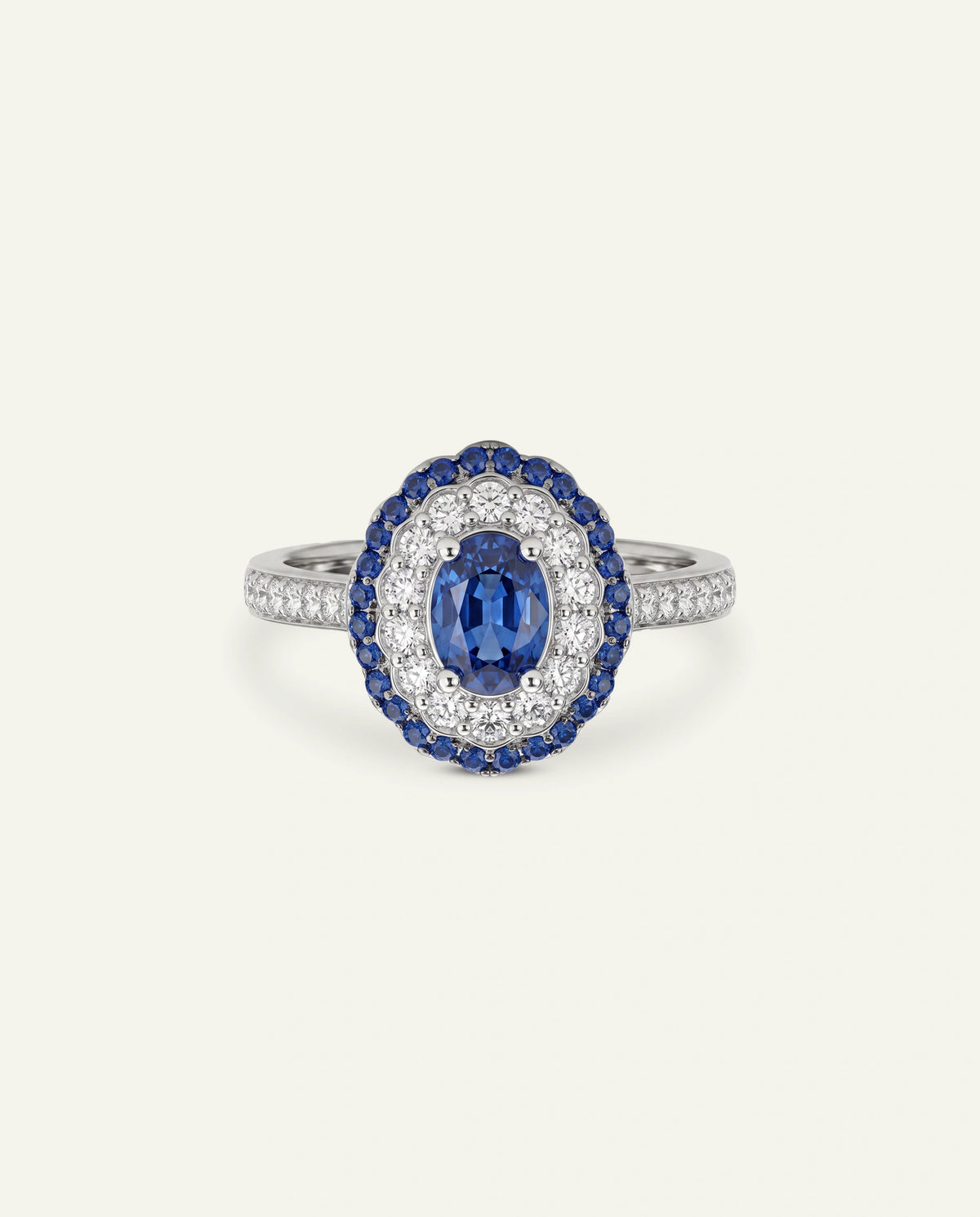 An oval halo ring featuring a central marquise-cut blue sapphire surrounded by a halo of small blue stones and a border of clear stones, set on a silver-toned band with pavÃ©-set clear stones, shown on a light cream background.