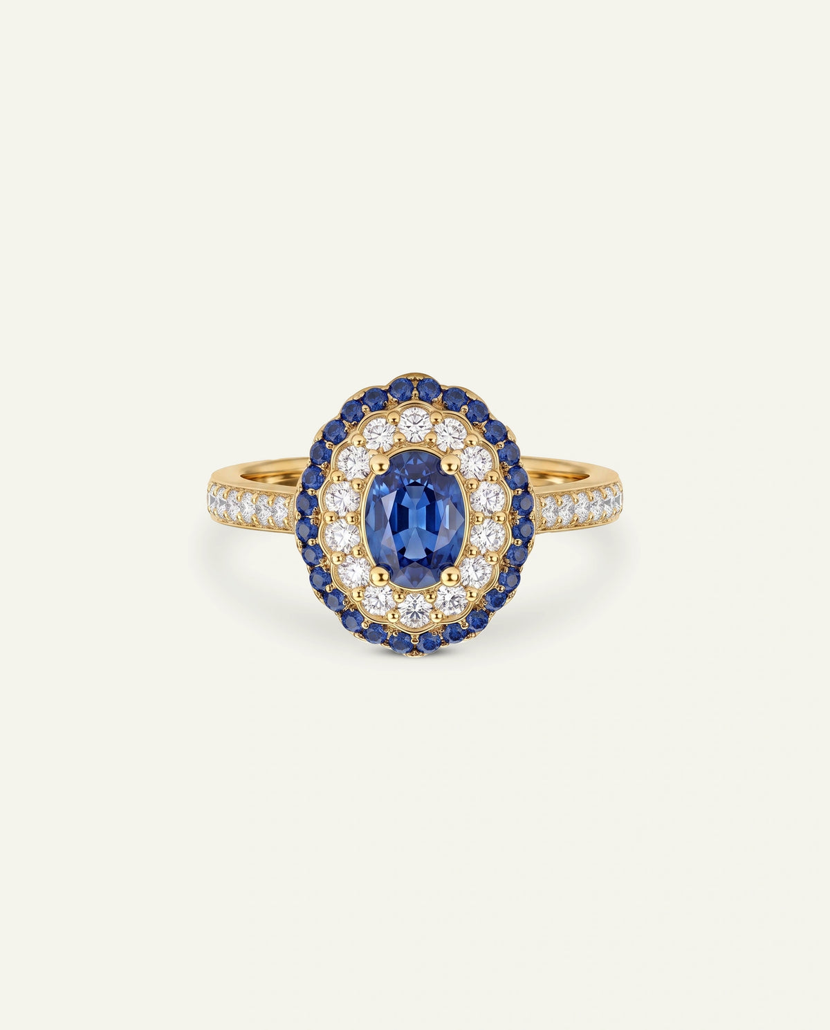 A yellow gold ring featuring an oval cluster setting with a central oval blue sapphire surrounded by a halo of small round blue sapphires and diamonds, with the band also paved with diamonds, set against a light off-white background.
