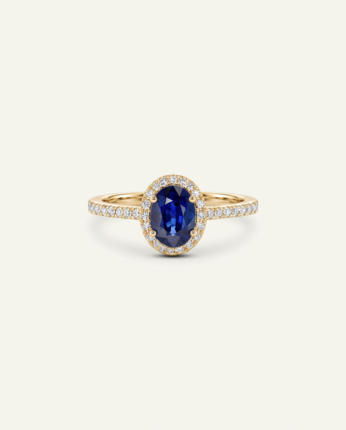 A yellow gold ring featuring an oval-cut deep blue sapphire center stone surrounded by a halo of small clear stones, with the band itself paved with tiny clear stones, set against a solid off-white background.