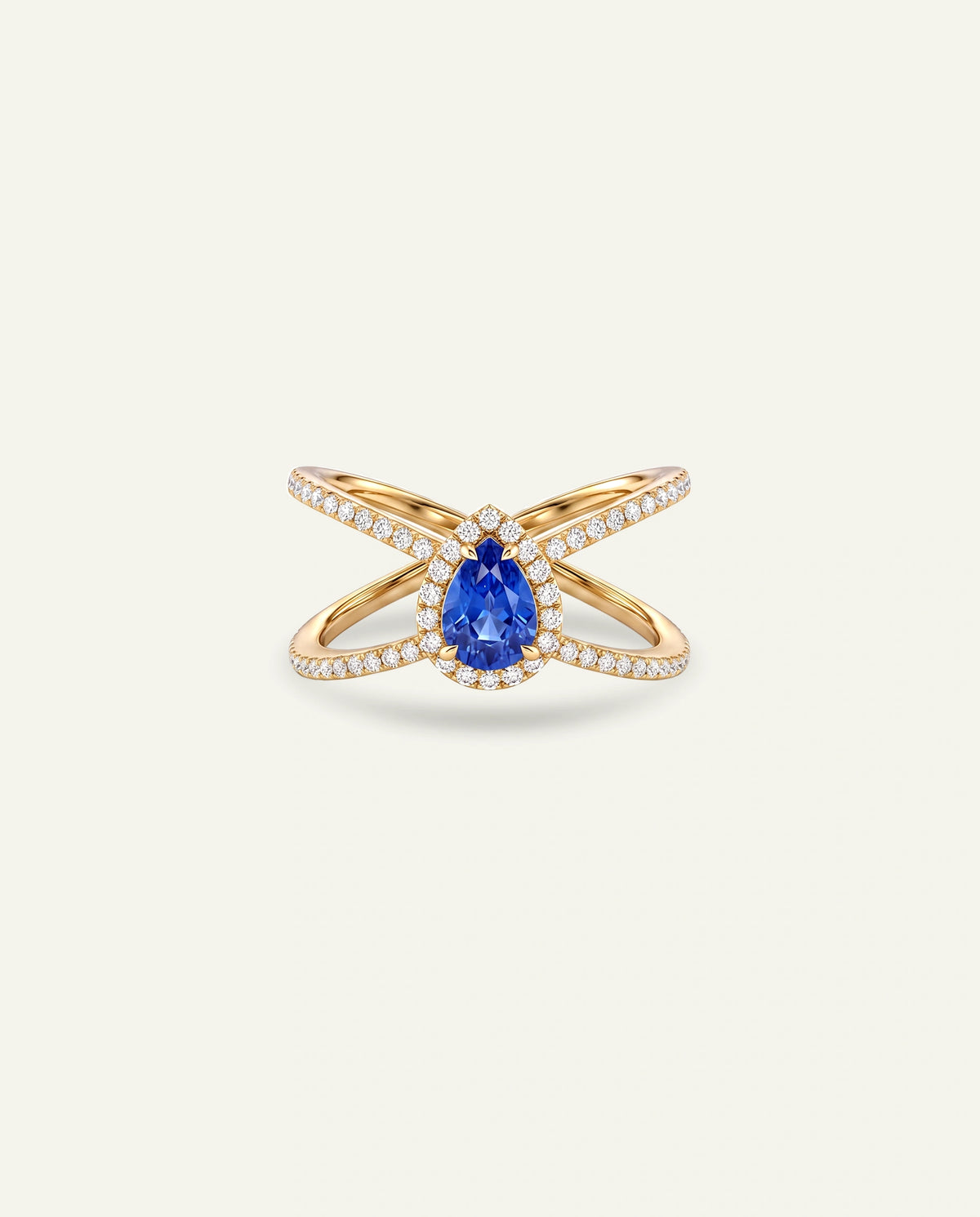 A gold ring featuring a central pear-cut blue sapphire gemstone surrounded by small clear stones, with two crossed bands also set with clear stones, on a light cream background.
