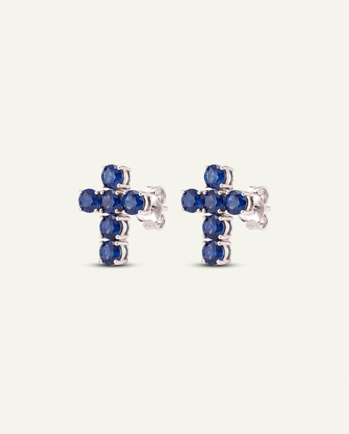 A pair of silver-toned cross stud earrings set with round blue gemstones, shown against a plain off-white background.