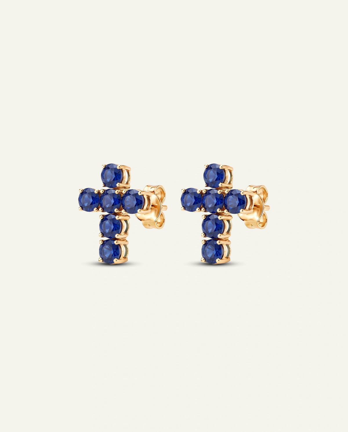 A pair of gold cross stud earrings set with round blue gemstones, shown against a plain off-white background.