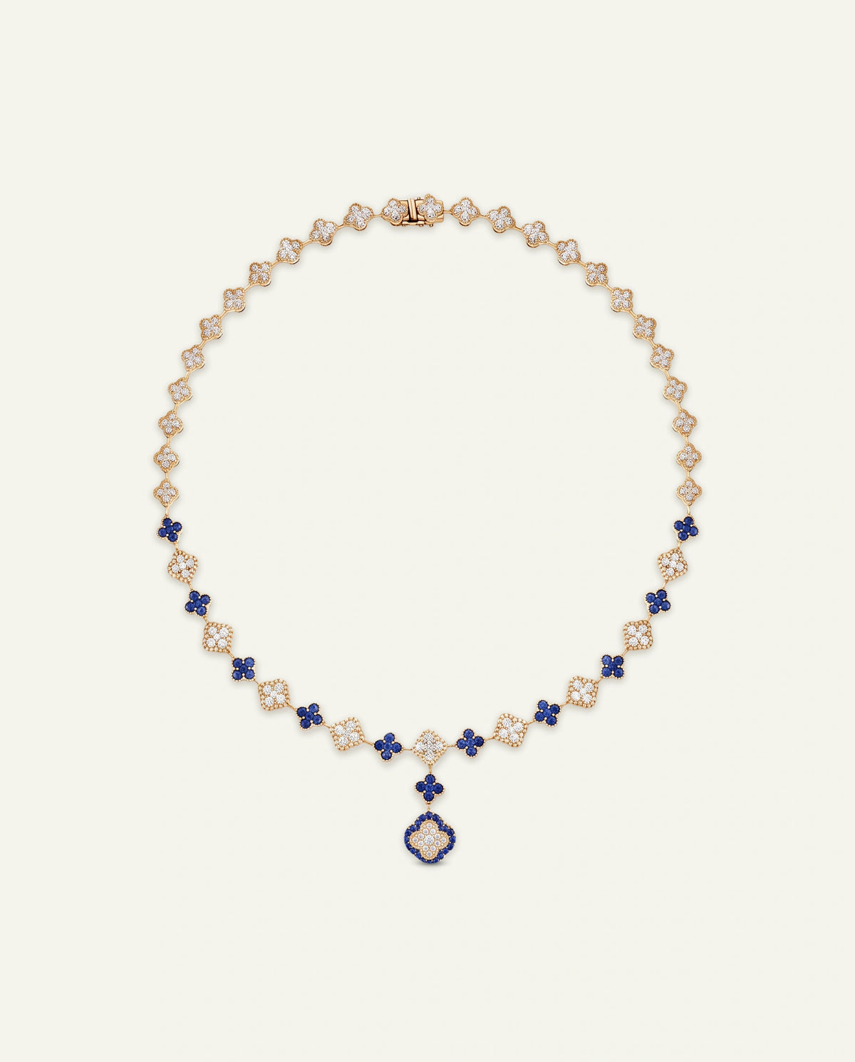 A luxury gold and diamond necklace with blue sapphire accents, featuring a signature clover motif and a central hanging clover pendant, displayed on a light cream background.