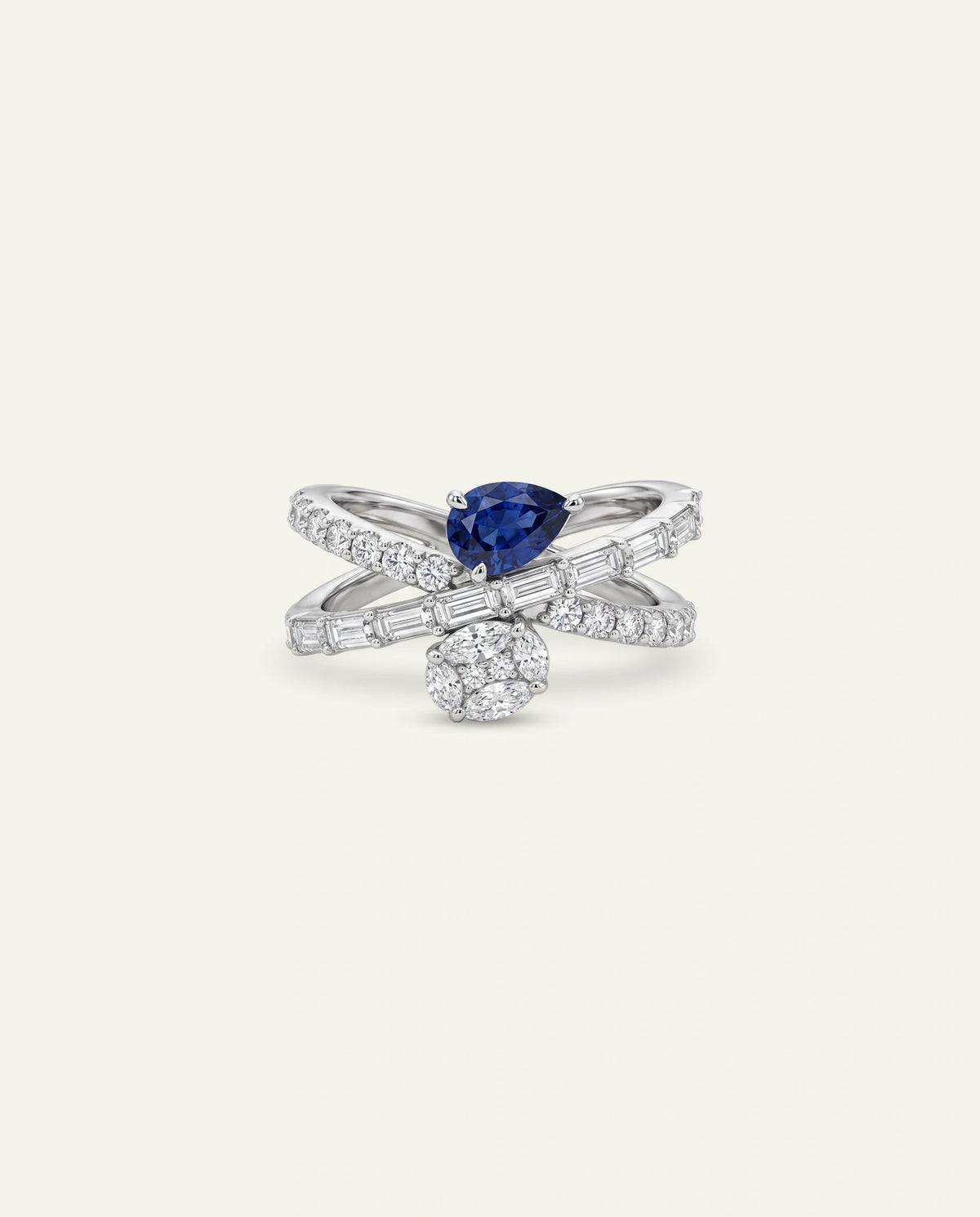 A silver-toned wrap ring featuring a pear-cut blue sapphire at the center, accented by pavÃ©-set diamonds and a round cluster of small diamonds, shown on a light cream background.