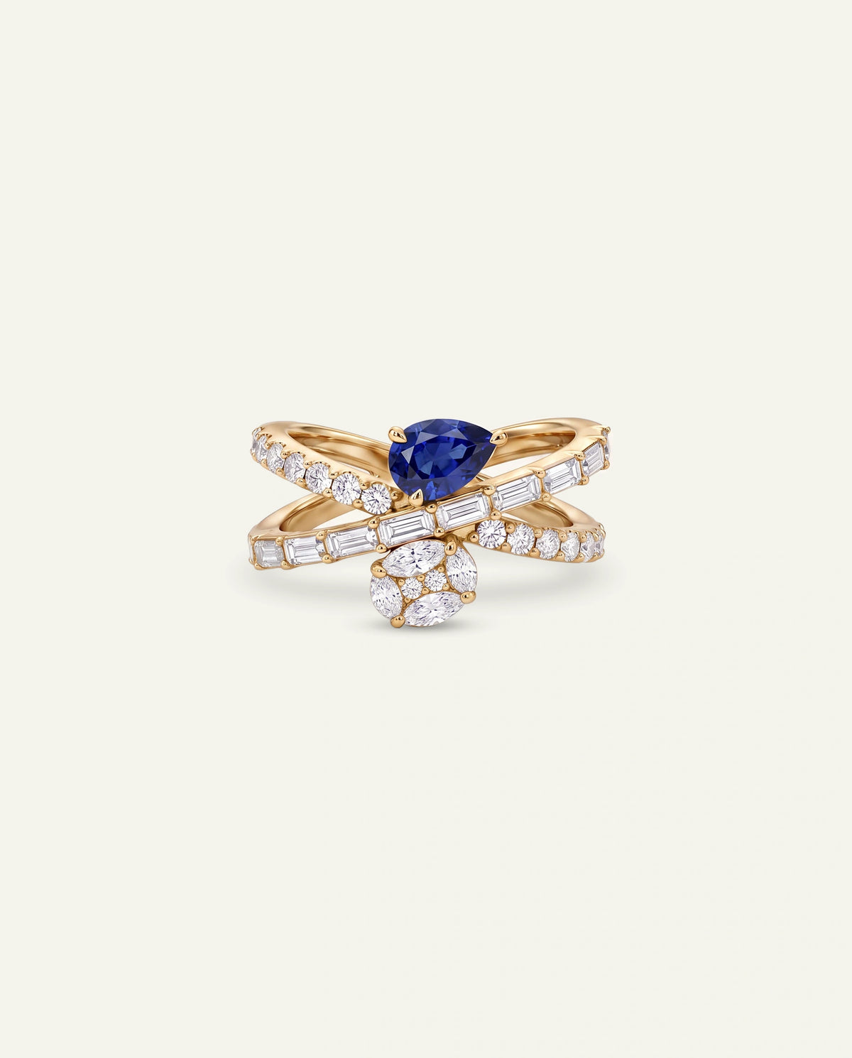 A gold ring featuring a pear-cut blue sapphire at the center, flanked by two curved bands paved with clear baguette and round diamonds, with a small cluster of clear stones below, set against a solid off-white background.