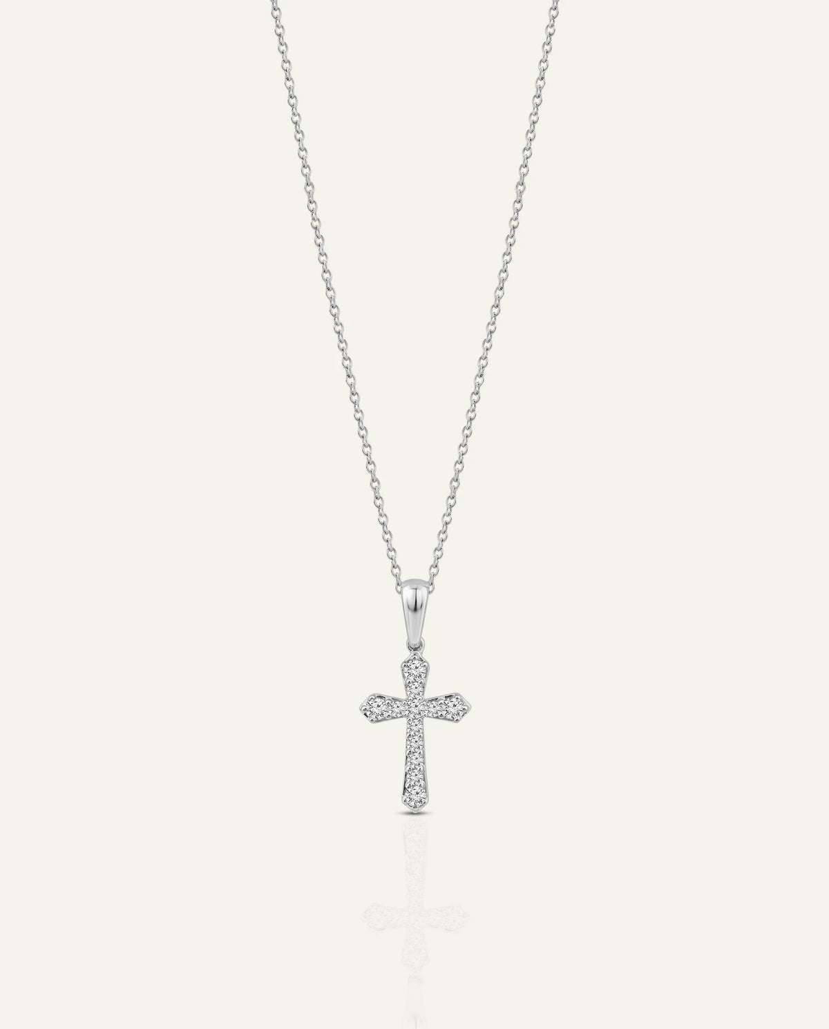 A silver cross pendant necklace adorned with small clear stones, suspended from a delicate silver chain against a light cream background.