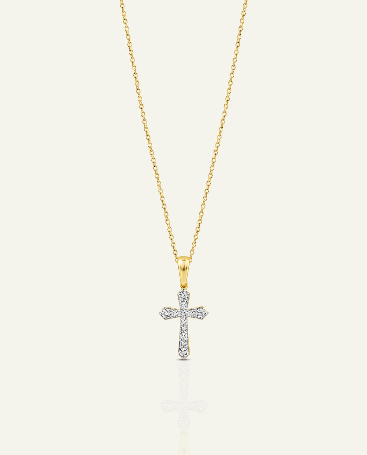 A delicate gold chain necklace with a cross pendant, where the right arm of the cross is paved with small clear stones, set against a light cream background.