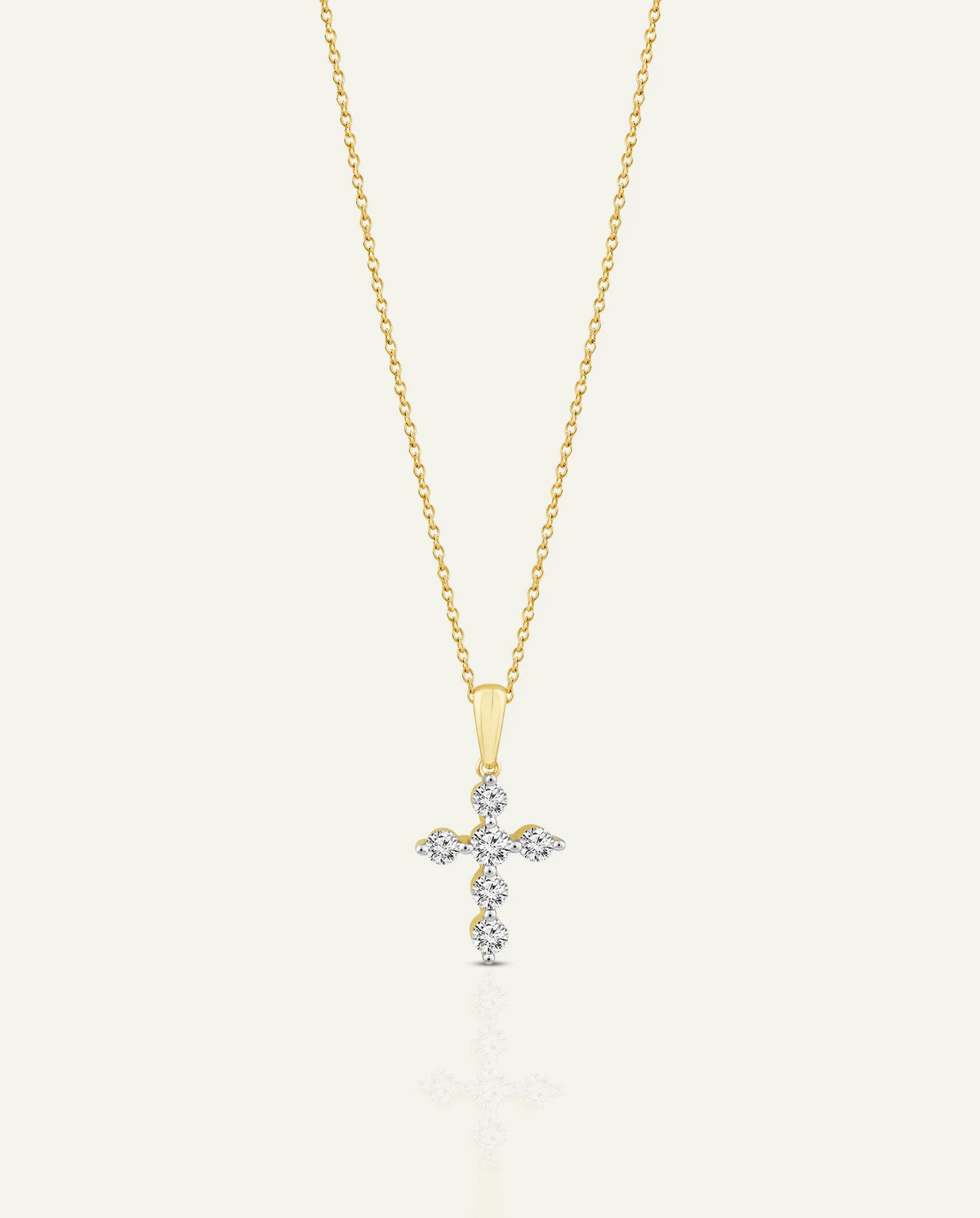 A delicate gold chain necklace with a small cross pendant adorned with clear gemstones, displayed against a light off-white background.