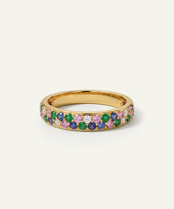 A gold band ring adorned with rows of round-cut gemstones in green, blue, pink, and clear pavé setting, photographed on a light cream background.