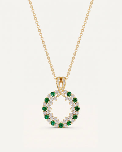 A gold necklace with a circular pendant featuring green and clear gemstones, displayed against a light off-white background.