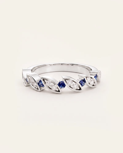 A silver-toned diamond and sapphire ring with marquise-cut and baguette-cut diamond settings, featuring alternating deep blue round sapphires and clear diamonds, shown on a light cream background. - alternate view