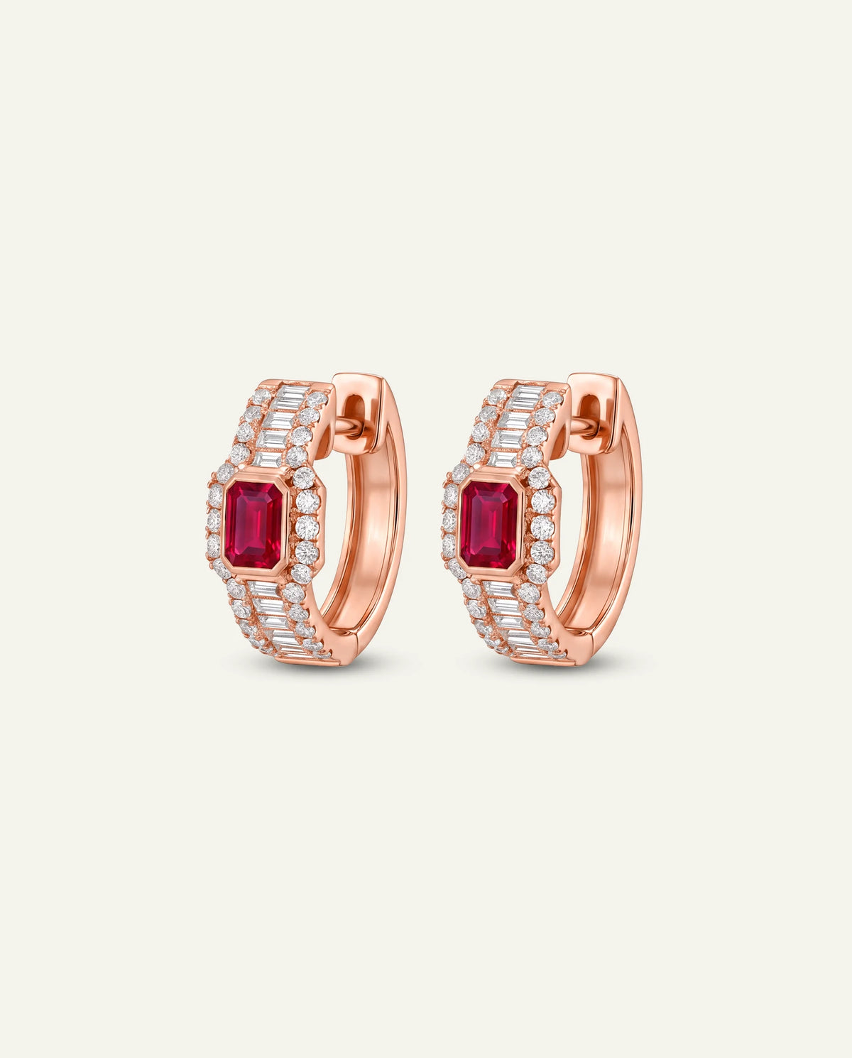 A pair of gold huggie hoop earrings featuring rectangular emerald-cut red ruby centers, surrounded by rows of small clear pavé stones, set against a light off-white background.
