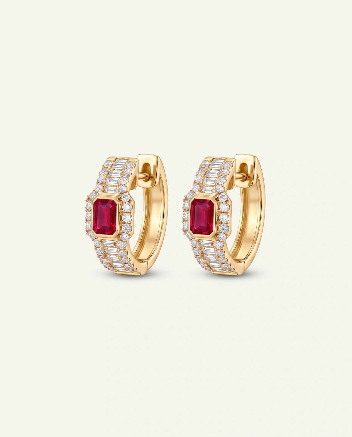 A pair of gold huggie hoop earrings featuring rectangular emerald-cut red ruby centers, surrounded by rows of small clear pavé stones, set against a light off-white background.