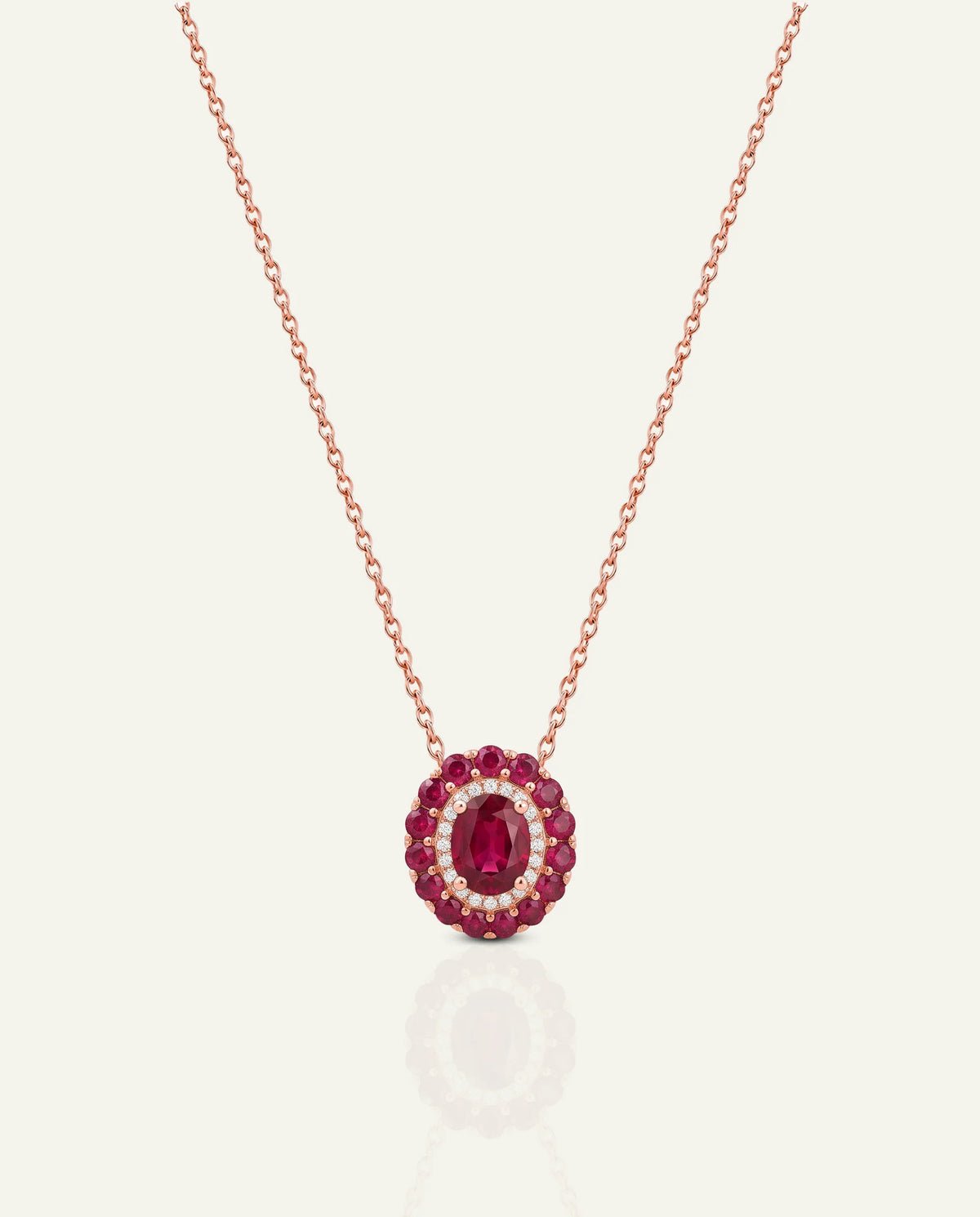 A rose gold necklace with a circular pendant featuring a central oval ruby gemstone surrounded by a halo of small clear stones and a border of round ruby gemstones, shown on a light cream background.