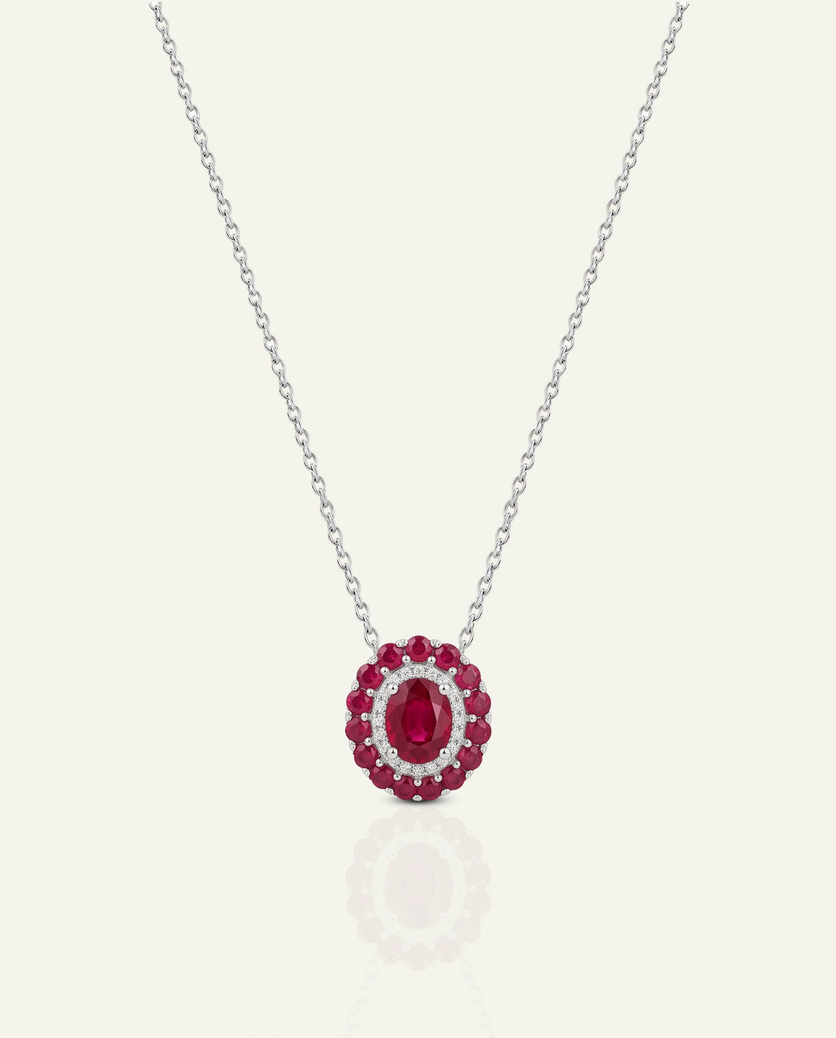 A silver chain necklace with a circular pendant featuring a central oval red gemstone surrounded by smaller round red and clear stones, shown on a light cream background.
