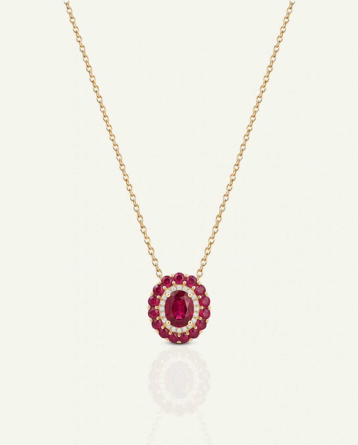 A gold pendant necklace featuring a circular design with a central oval ruby-red gemstone surrounded by smaller round ruby and clear crystal accents, suspended on a delicate gold chain against a light cream background.