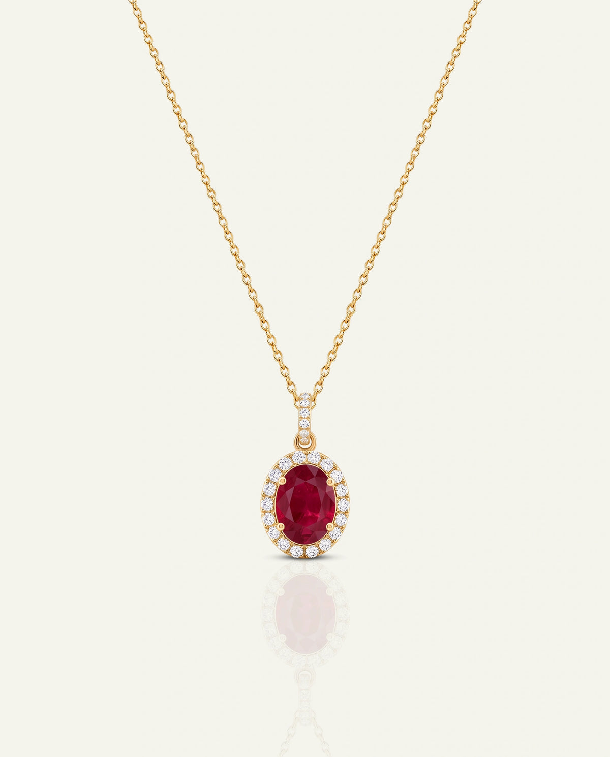 A gold chain necklace with an oval red gemstone pendant, surrounded by a halo of small clear stones, shown on a light cream background.