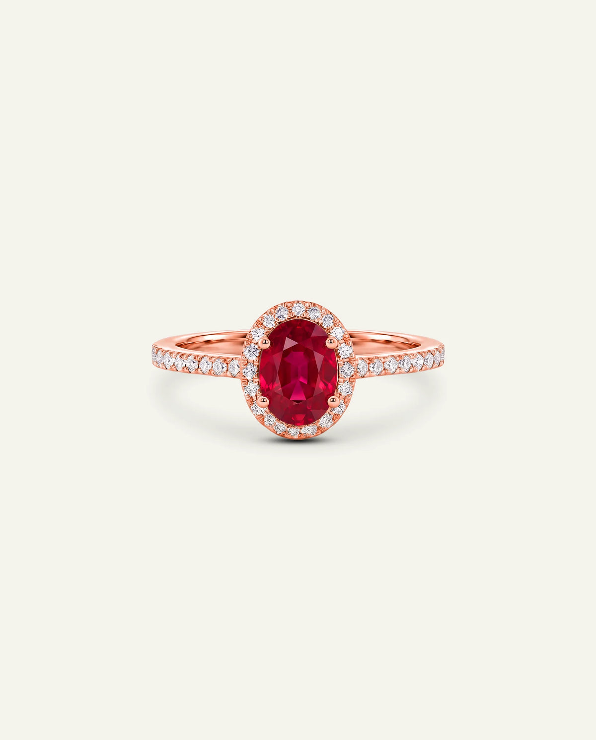 A rose gold ring featuring an oval-cut red ruby center stone surrounded by a halo of small clear stones, with the band itself paved with clear stones, set against a solid off-white background.